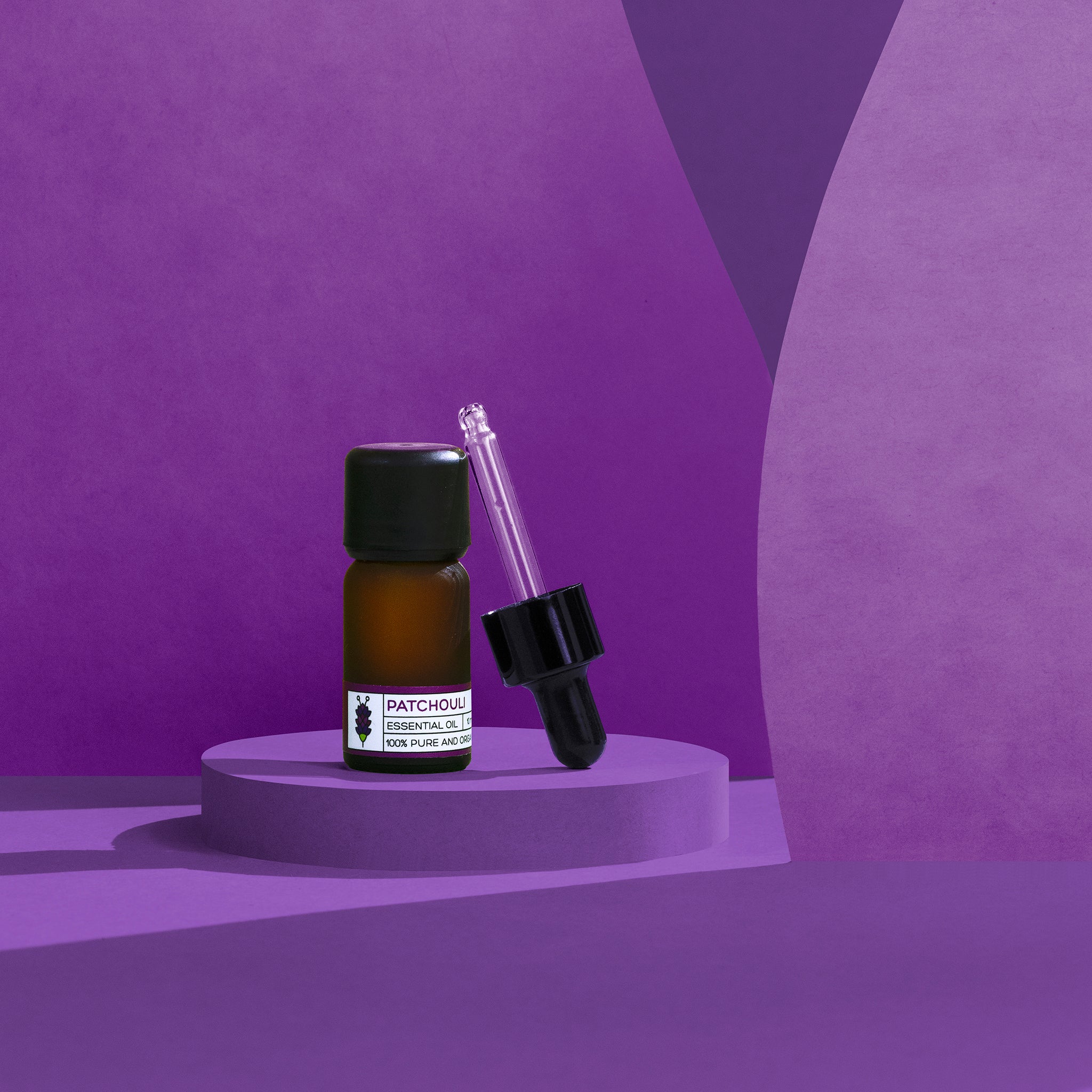 Patchouli Essential Oil Amber glass bottle with dropper on a purple platform against a matching purple background