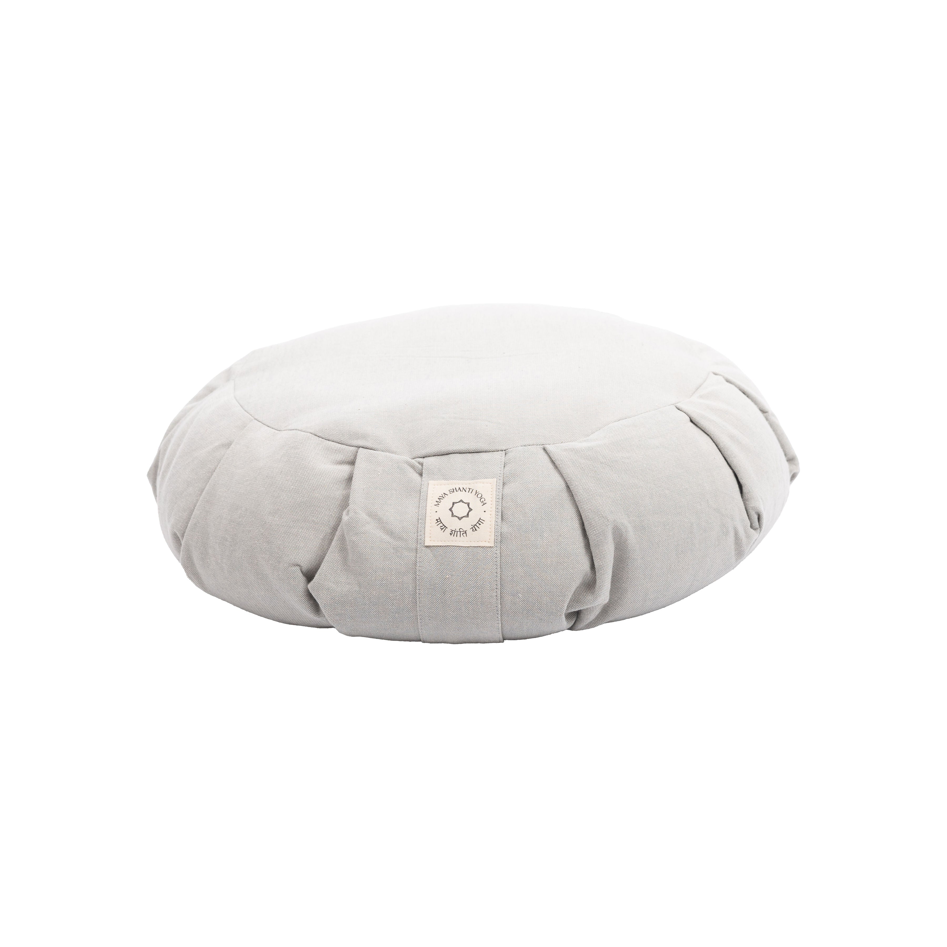 The MSY Zafu - Ice Grey by Maya Shanti Yoga is a round, gray meditation cushion filled with organic buckwheat hulls and has a small label on the side, elegantly resting on a pristine white background.