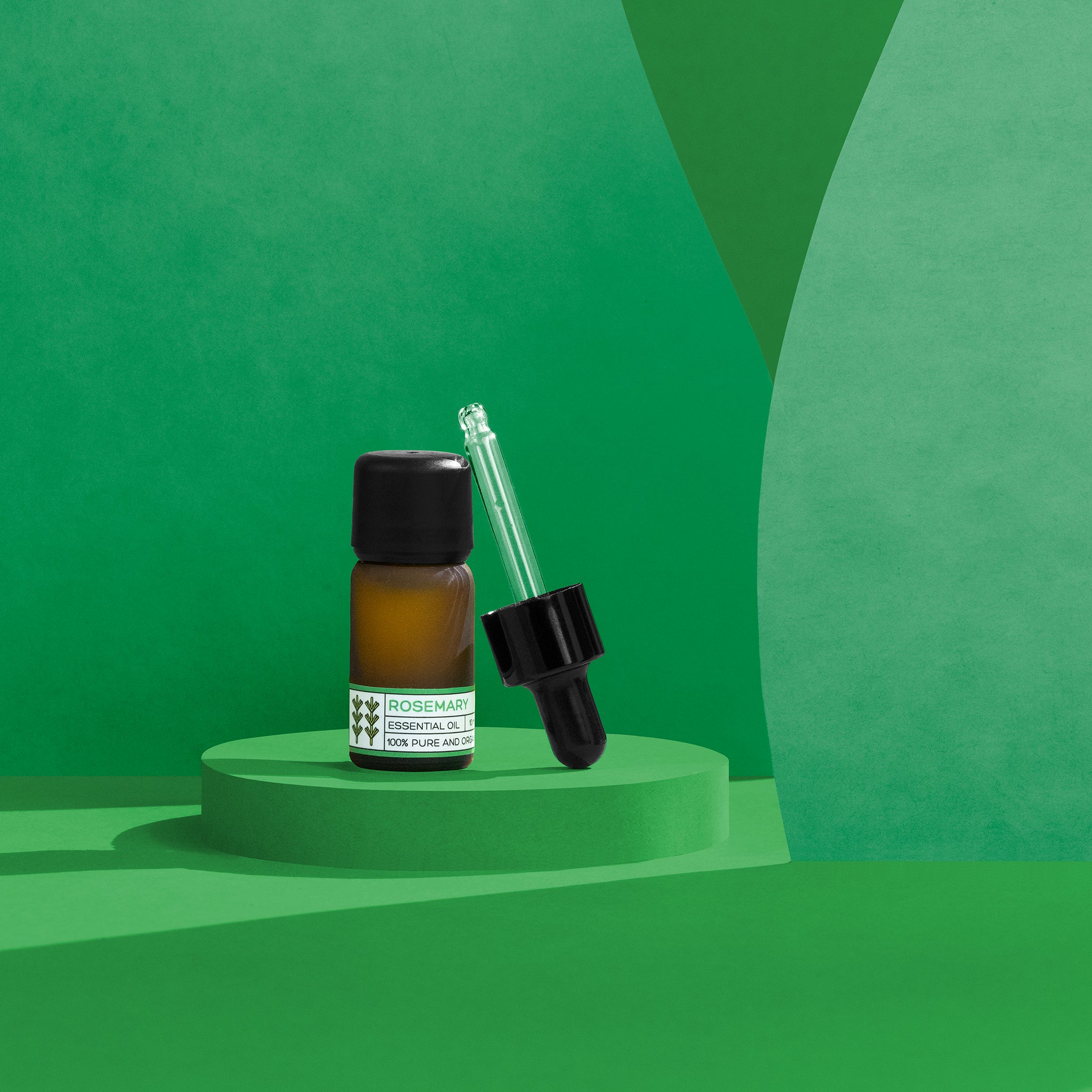 Bottle of rosemary essential oil with dropper on a green geometric background