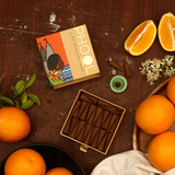 Phool Orange Incense Cones open packaging with a cone in a holder and cut and whole oranges on a dark wood background.