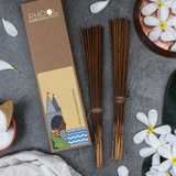 Phool Nagchampa incense sticks refill pack box next to 2 bundles of incense sticks surrounded by white flowers on a grey textured surface.