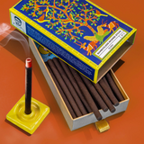 Phool Oudh Bambooless Incense sticks box open with sticks exposed and a lit incense stick next to it on an orange background.