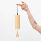 Hand holding a MSY wooden earth element chime from the loop against a white background.