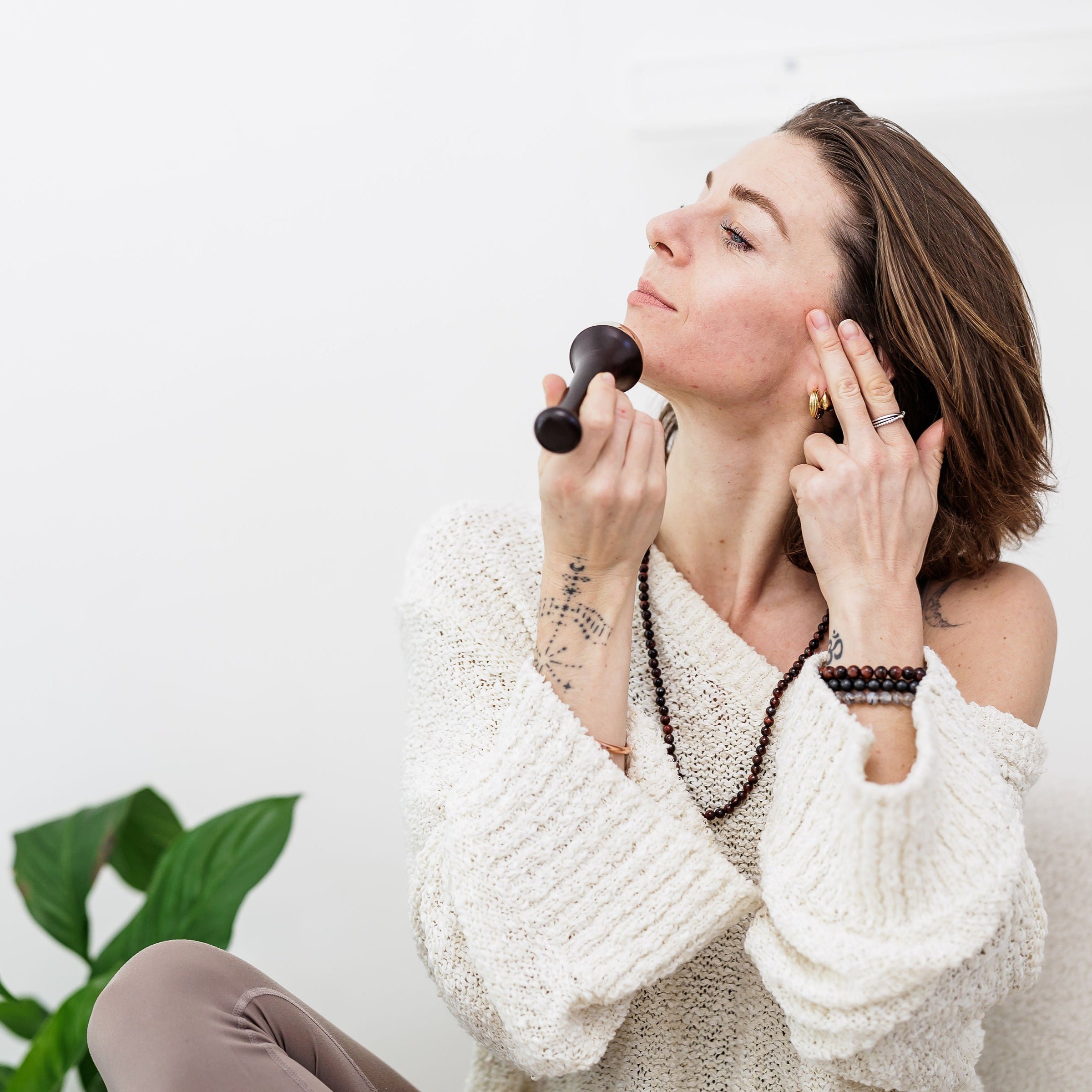 A woman holding a Black MSY Ayurvedic Kansa Wand to her face, with her side profile to the camera.