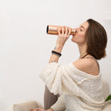 Woman drinking from a Maya Shanti Yoga Hammered Copper 750ml Water Bottle with her eyes closed.