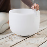 A person is playing a Maya Shanti Yoga MSY Crystal Singing Bowl from the Set of 3 (432 Hz) with a mallet on a wooden floor, creating soothing tones perfect for sound healing.