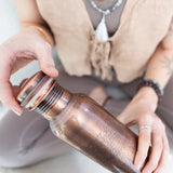 Close-up of a person holding a Maya Shanti Yoga Copper Etched 750ml Water Bottle in 1 hand while screwing on the lid with the other.