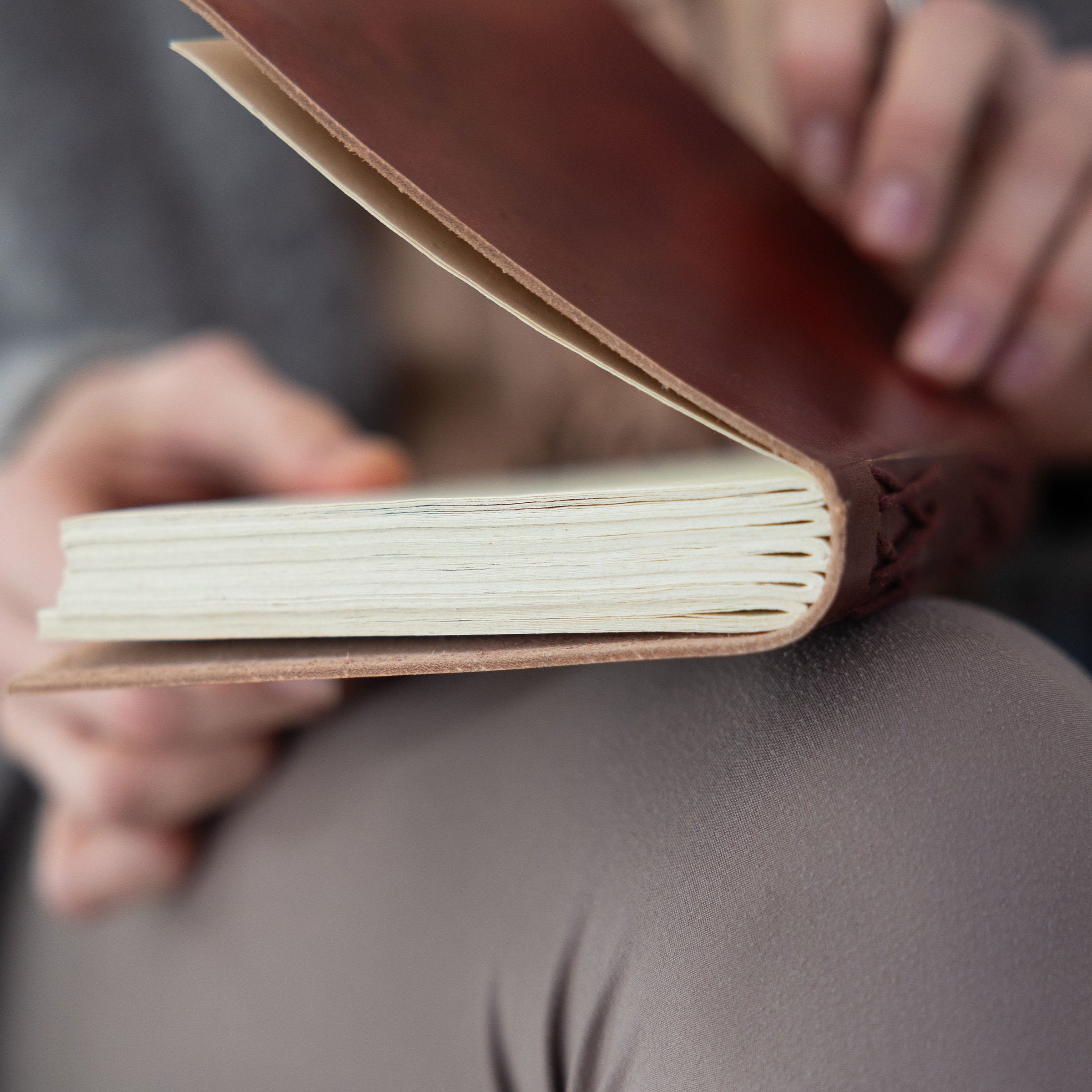 Brown leather-bound book held open by hands with a blurred background
