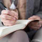 Person writing in a MSY Handmade Leather Journal with a ballpoint pen with their body blurred in the background.