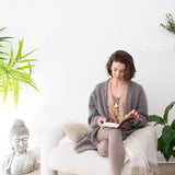 Woman reading her MSY Handmade Leather Journal on a white couch with plants and a Buddha statue in the background.