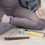 Phool Patchouli Incense Stick burning in holder on a wooden floor with a person sat cross-legged behind it.
