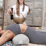 Two women practicing mindfulness, laying down on a Maya Shanti Yoga Small Bolster and using a sound healing instrument.