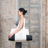 A woman carrying a yoga mat in a  MSY Yoga Totebag - Cotton from Maya Shanti Yoga.