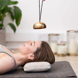 Woman lying on a MSY rubber jute yoga mat and yoga pillow with a MSY Hanging Himalayan Singing Bowl above their head.
