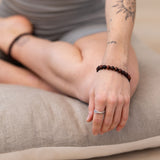 Person sitting cross-legged on a MSY Zabuton Meditation Cushion with arm resting on knee wearing a Tiger Eye Mala Bracelet on the wrist.