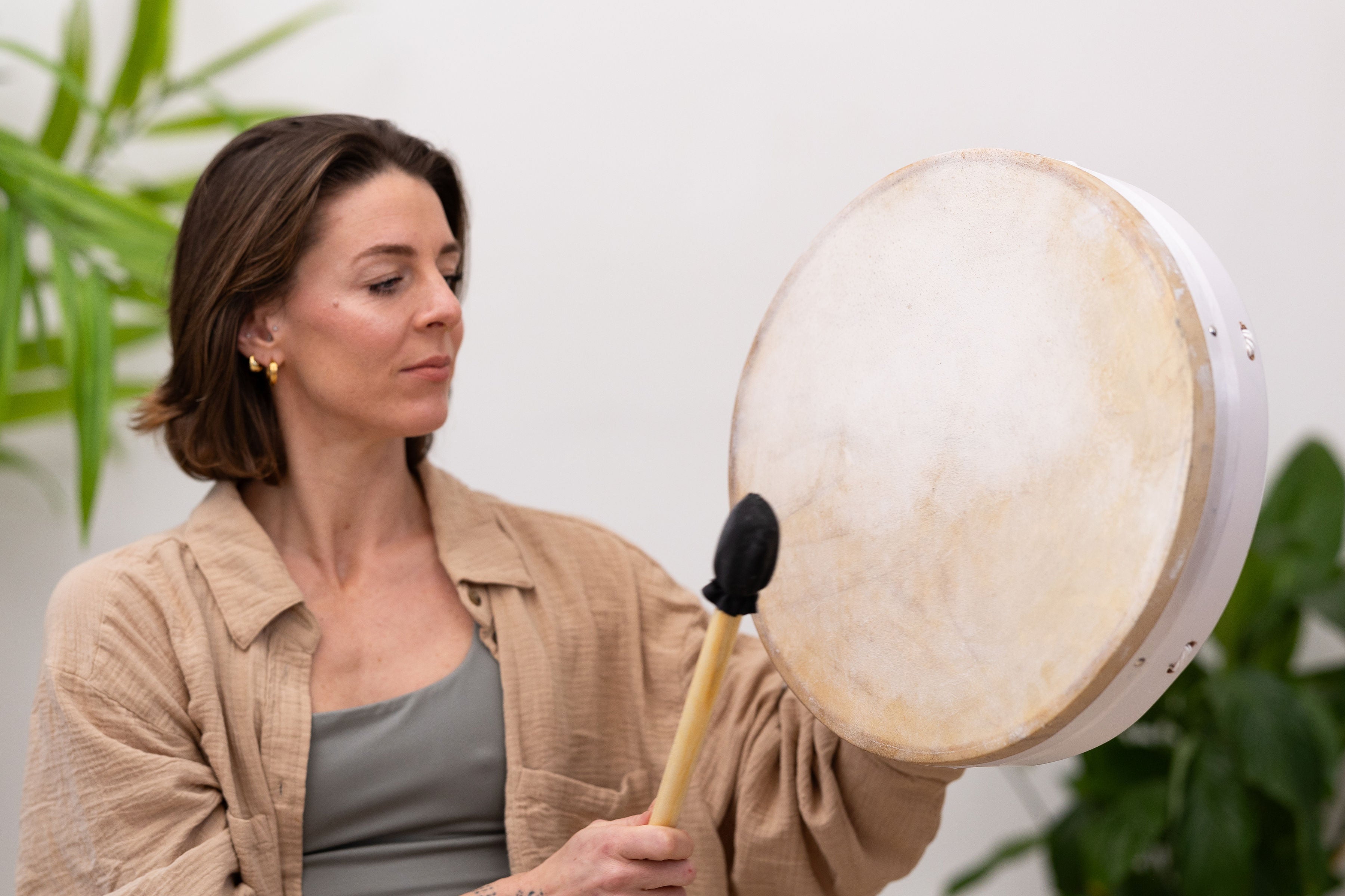 Woman holding MSY Buffalo Drum and drumstick, looking towards it with a soft expression.