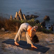 Person practising yoga on a MÄTi Pro Yoga Mat with the ocean and rocks in the background