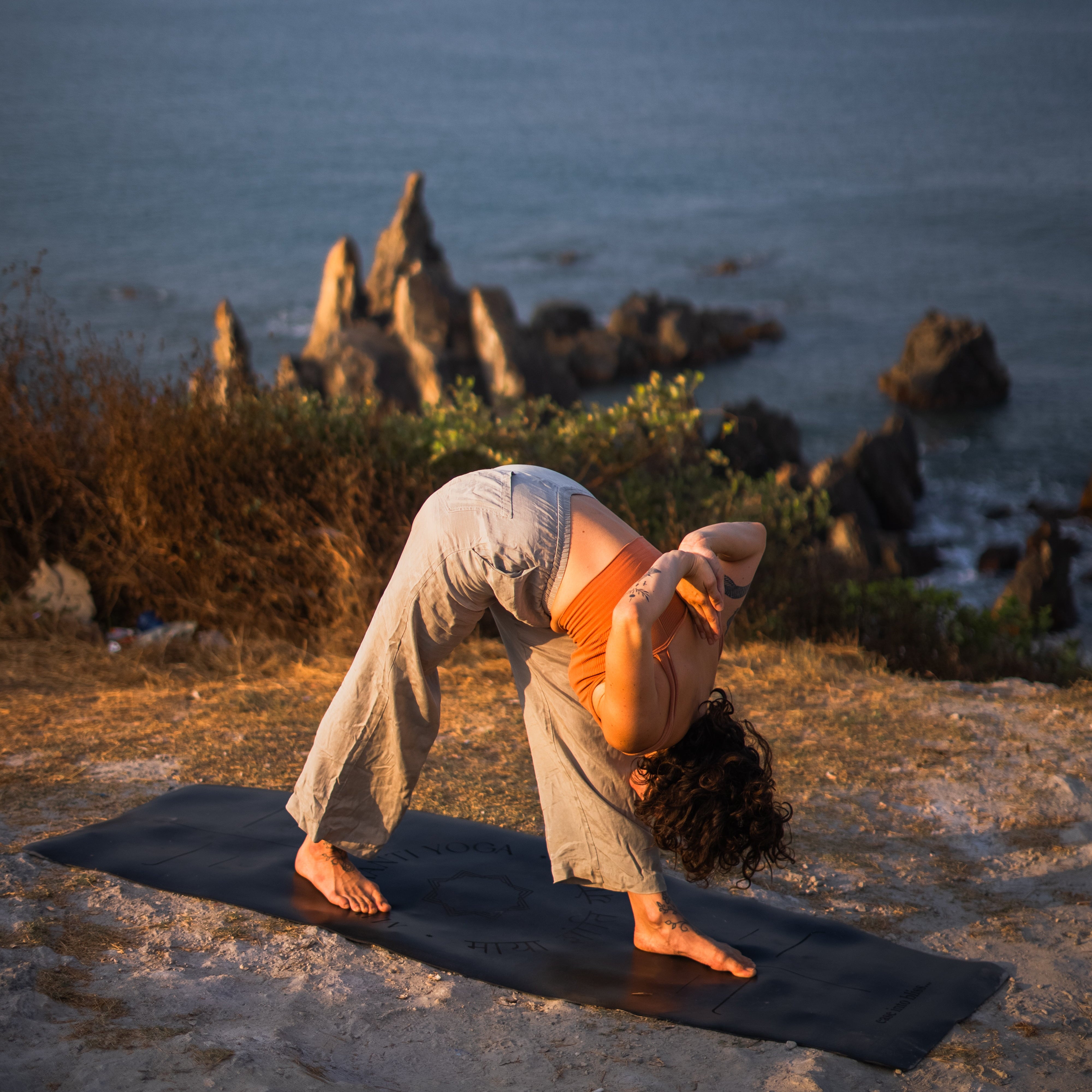 Person practising yoga on a MÄTi Pro Yoga Mat with the ocean and rocks in the background