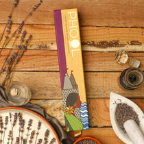 A box of Maya Shanti Yoga Phool Incense - Lavender, crafted with essential oils, rests on a wooden surface surrounded by dried lavender, a mortar and pestle, and a glass bottle.