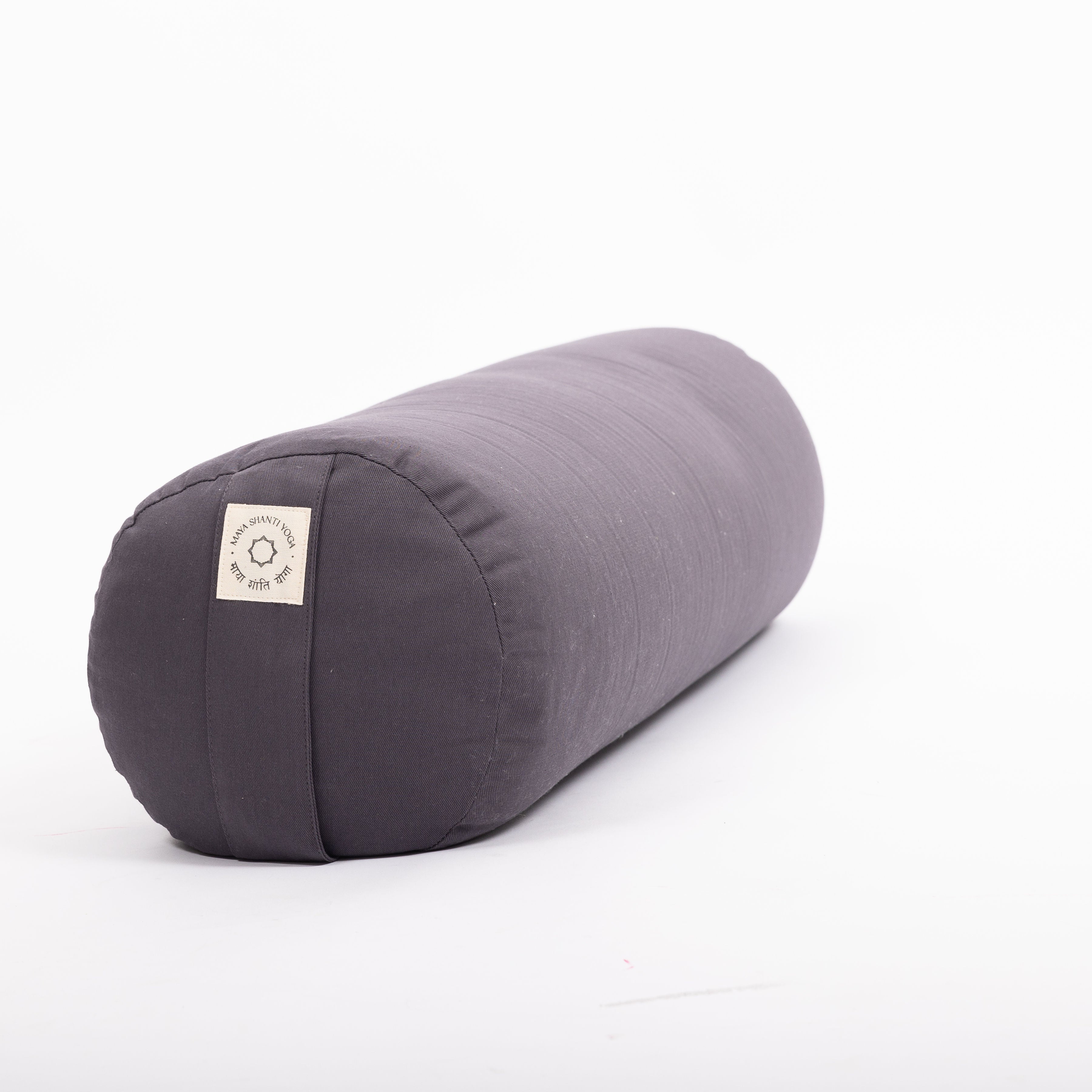 The MSY Large Round Buckwheat Bolster in Anthracite Grey by Maya Shanti Yoga is eco-friendly and perfect for yoga. It rests on a white background, boasts a small fabric label, and is designed for comfort and sustainability.