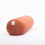 The MSY Large Round Buckwheat Bolster in Rust by Maya Shanti Yoga, featuring a white label on one end, sits on a white background. This eco-friendly bolster offers perfect yoga support for mindful practice.