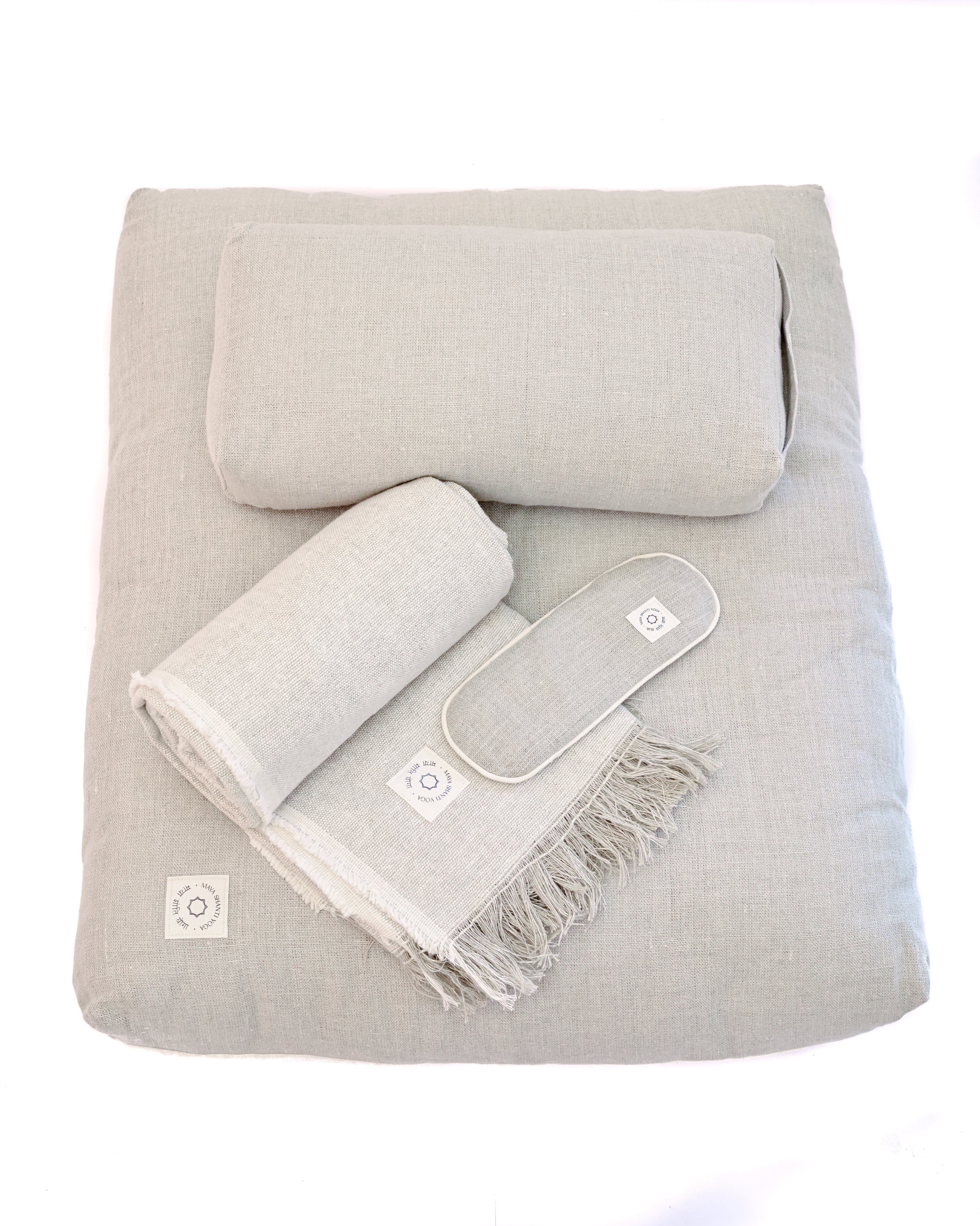 A set of MSY Serenity Bundle including small bolster, zabuton, blanket and eyepillows on a white surface, perfect for mindfulness and meditation, by Maya Shanti Yoga.