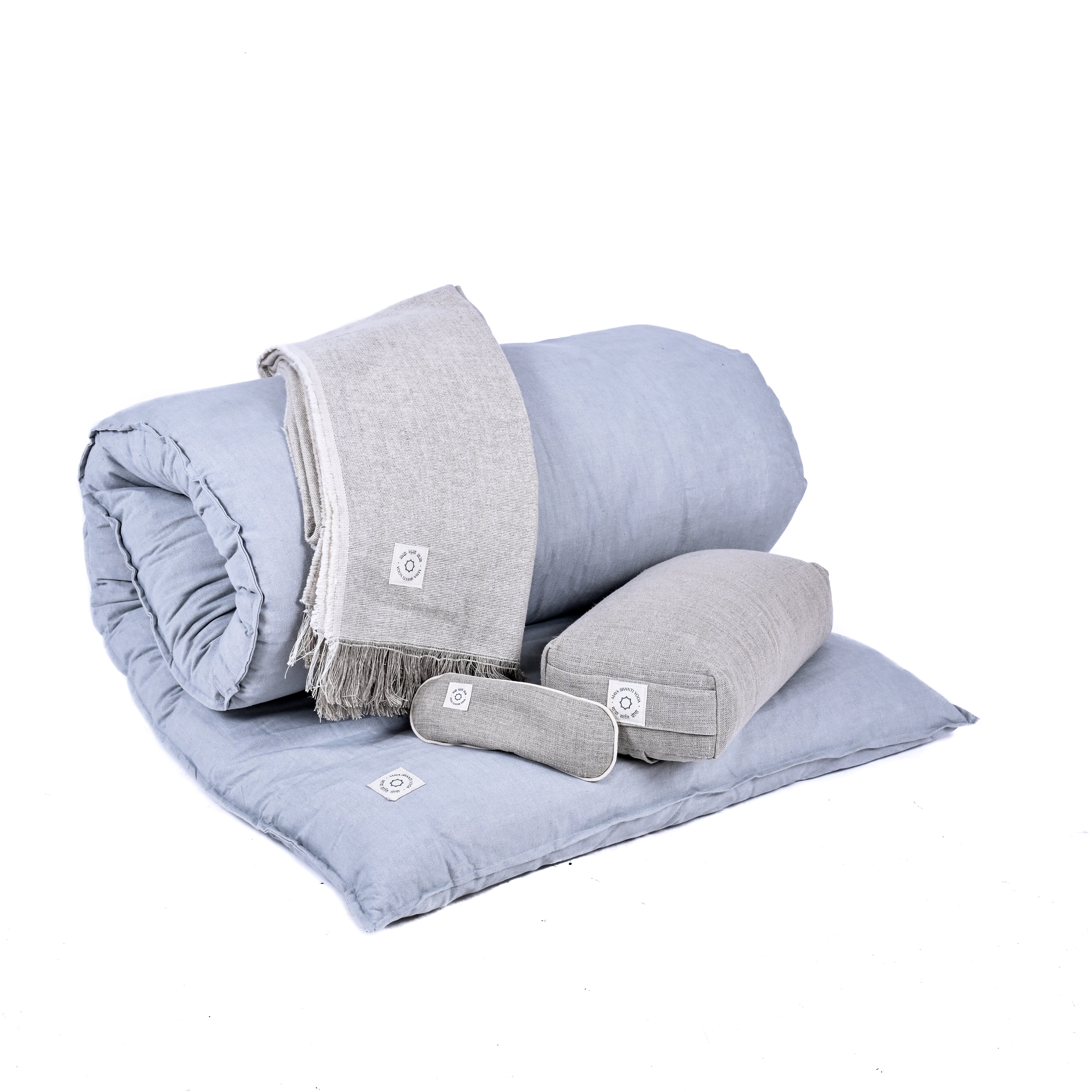 A neatly folded set of light blue bedding including a duvet, a large pillow, a small bolster pillow, and a folded grey blanket lies on the display. The MSY Tranquillity Bundle from Maya Shanti Yoga adds a touch of serenity to any space.