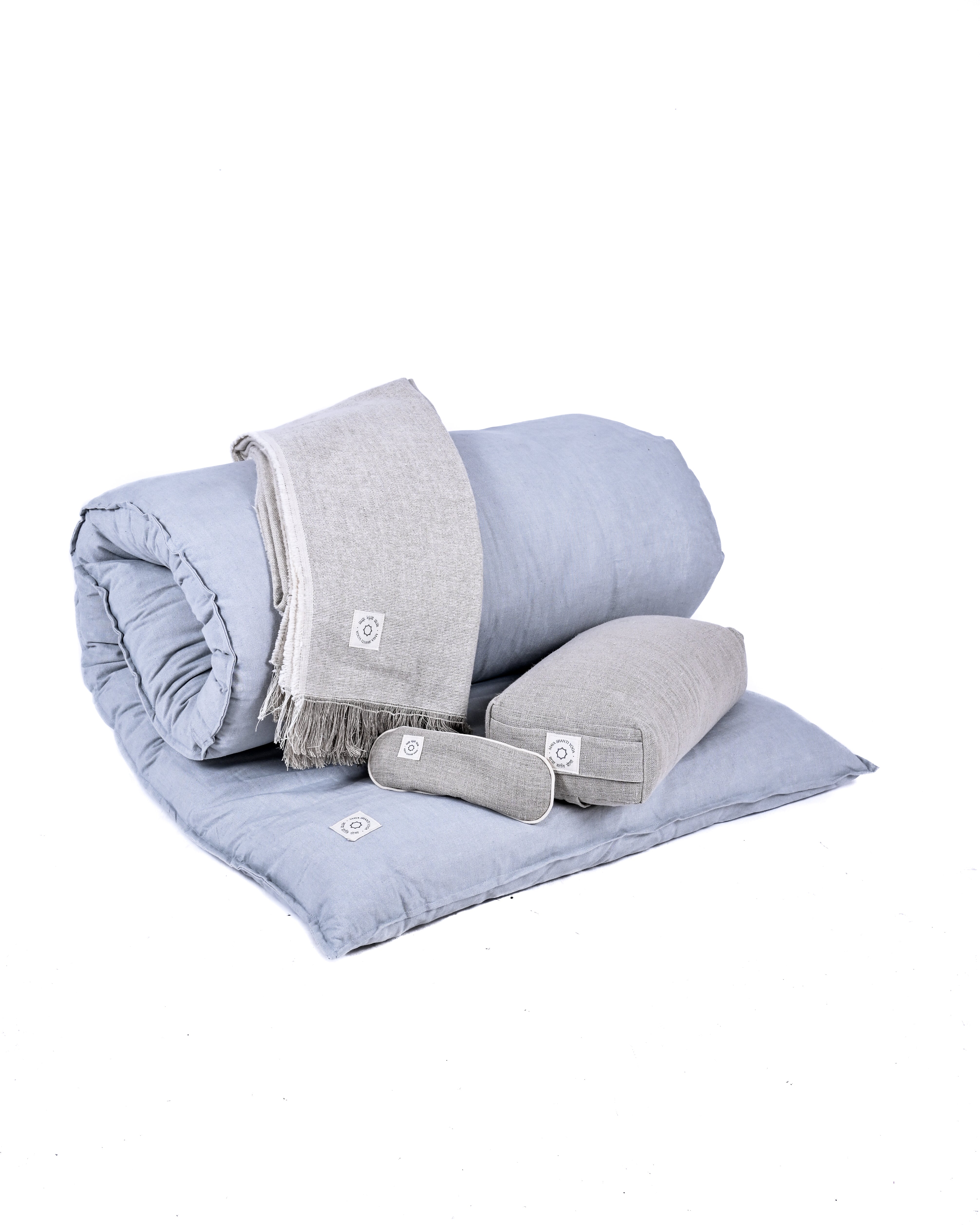 A neatly folded set of light blue bedding including a duvet, a large pillow, a small bolster pillow, and a folded grey blanket lies on the display. The MSY Tranquillity Bundle from Maya Shanti Yoga adds a touch of serenity to any space.