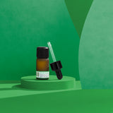 Bottle of rosemary essential oil with dropper on a green geometric background