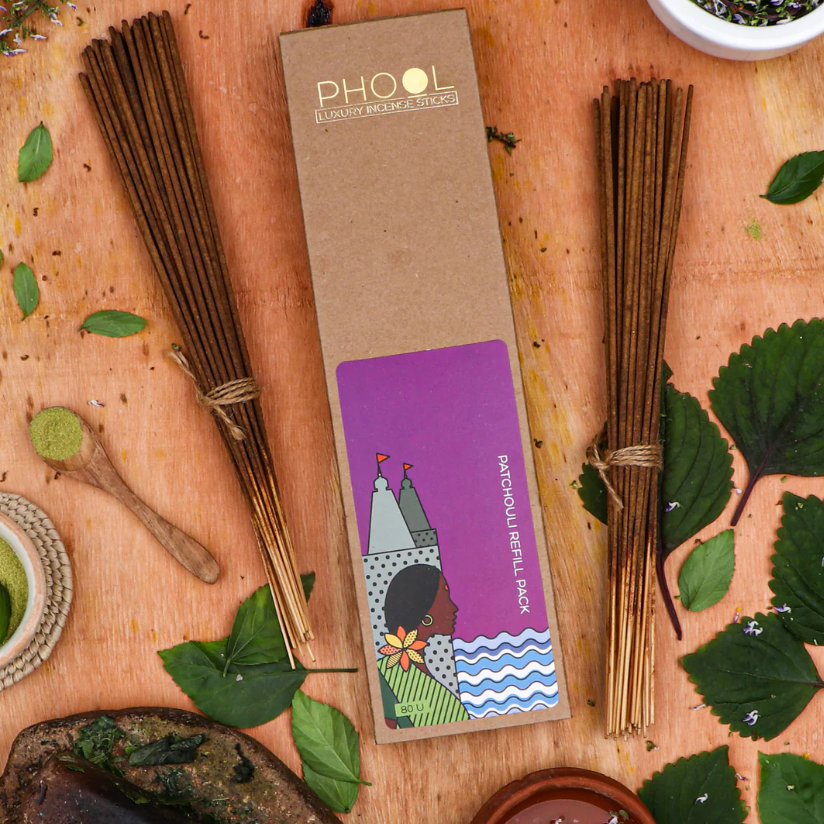 Two bundles of incense sticks with a 'PHOOL' packaging box on a wooden surface with green leaves.