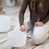 Person kneeling on MSY bolster using two rubber mallets to create sounds on a crystal singing bowl.