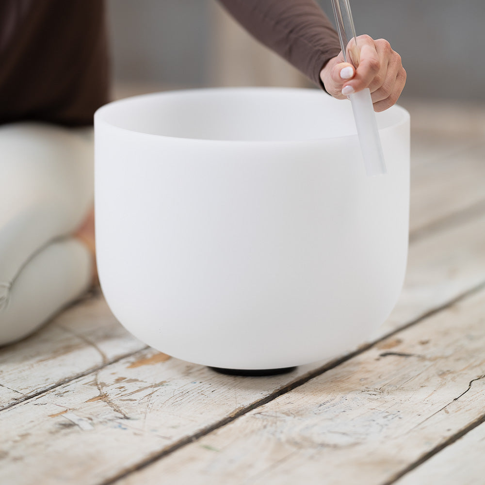 A woman is sitting on a wooden floor, practicing mindfulness with the Maya Shanti Yoga Crystal Bowls supported on an O-Ring by Maya Shanti Yoga.