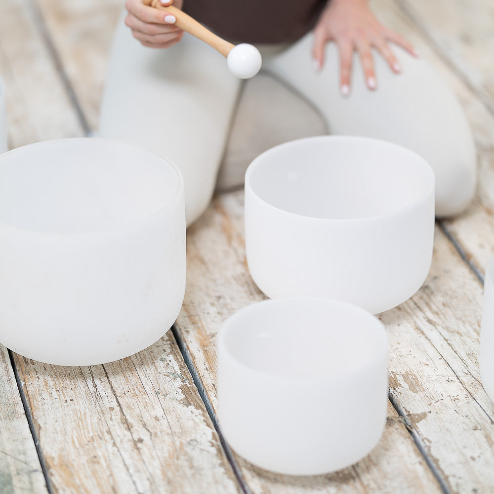 A woman is sitting on a wooden floor with Maya Shanti Yoga's MSY Rubber Mallets For Crystal Bowls - Set of two, engaging in mindfulness practices.