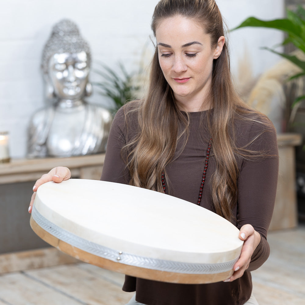 A woman practicing mindfulness while holding up a MSY Ocean Drum - 18inch by Maya Shanti Yoga.