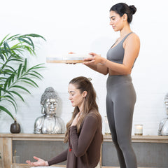 A woman practicing mindfulness and meditation, using a Maya Shanti Yoga 18inch Ocean Drum while sitting in front of another woman.