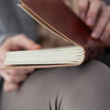 Brown leather-bound book held open by hands with a blurred background