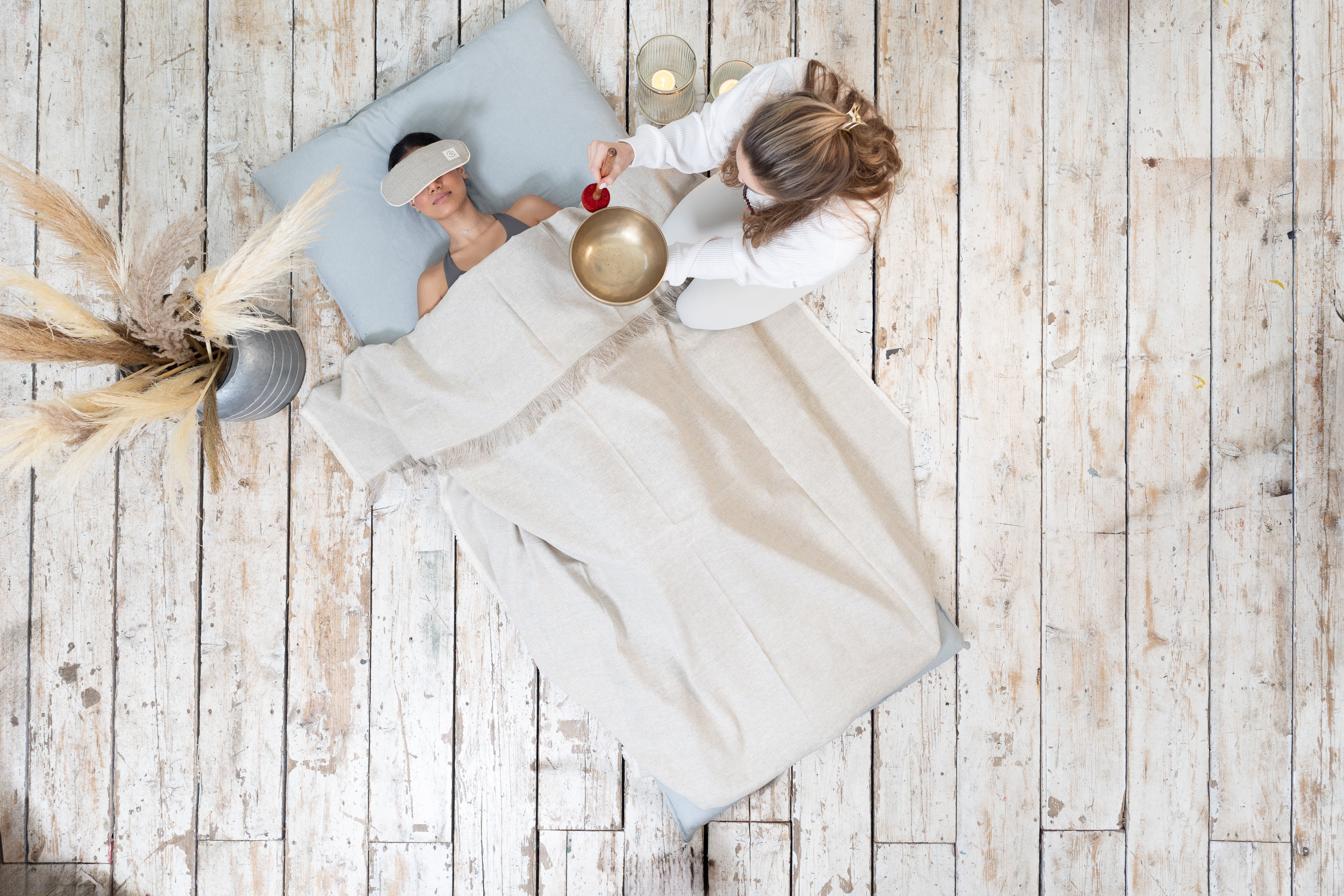 A woman lying on a shatsu with a blanket and bolsters on a wooden floor.