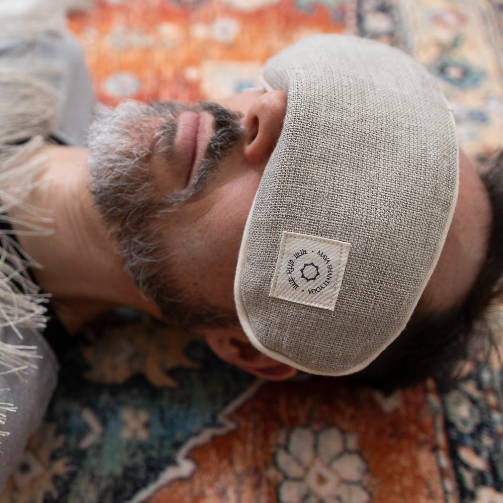 A man practicing meditation while lying on the floor with a Maya Shanti Yoga Lavender Eye Pillow - Hemp, Lavender & Linseed.