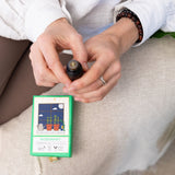 Person holding a small green bottle of rosemary essential oil sitting on a beige couch.