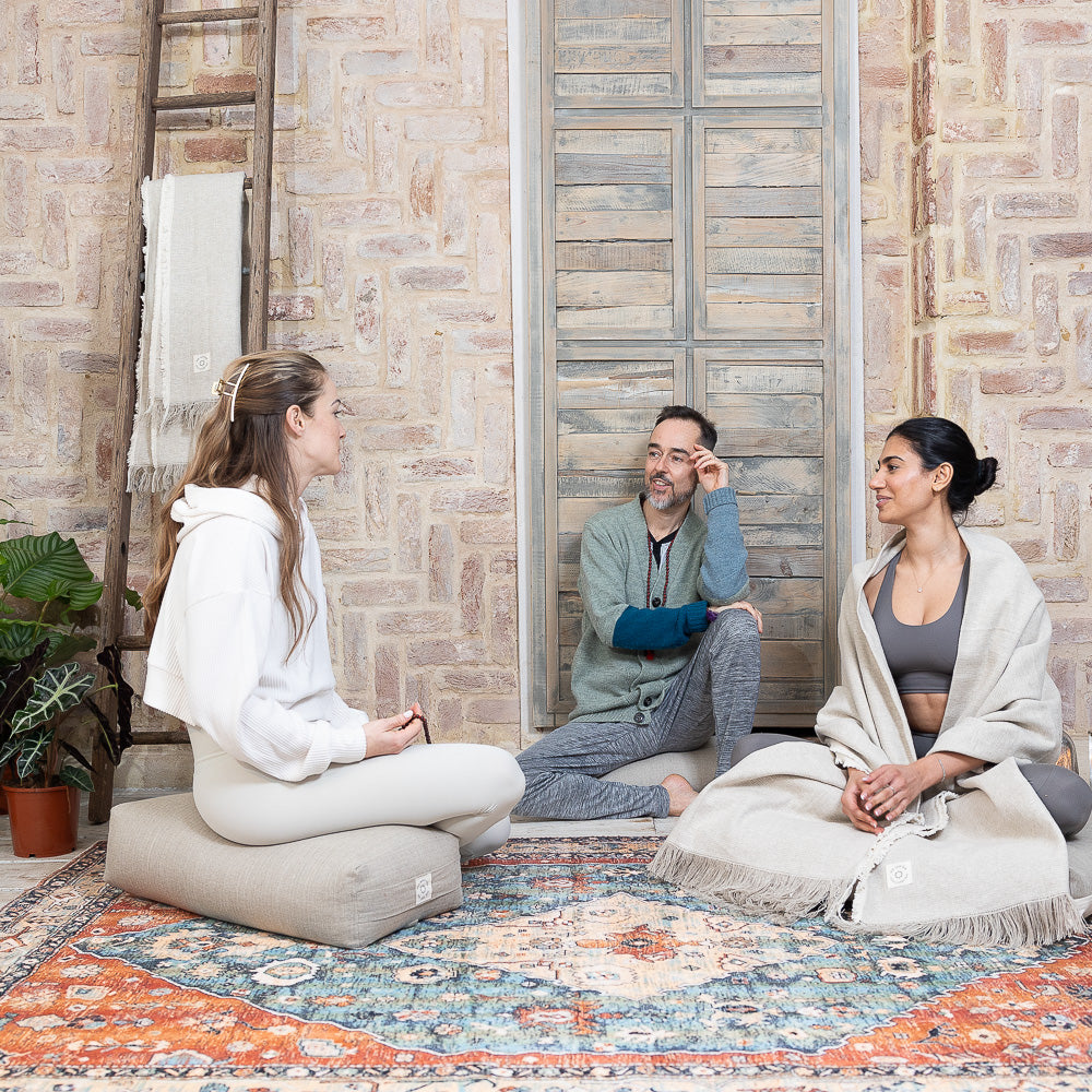 Three people sitting on a colorful rug in a room with stone walls and a ladder.
