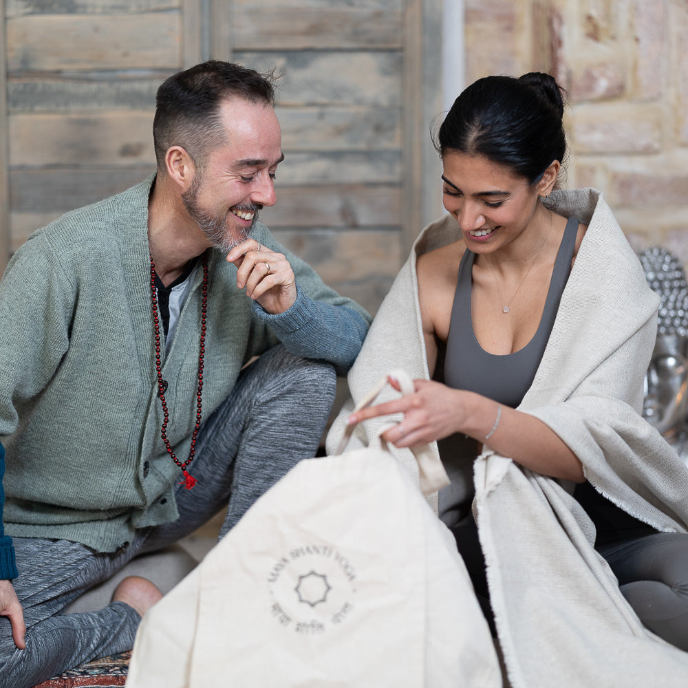 A man and woman smiling and talking while sitting on a rug with a Maya Shanti Yoga Totebag - Cotton.
