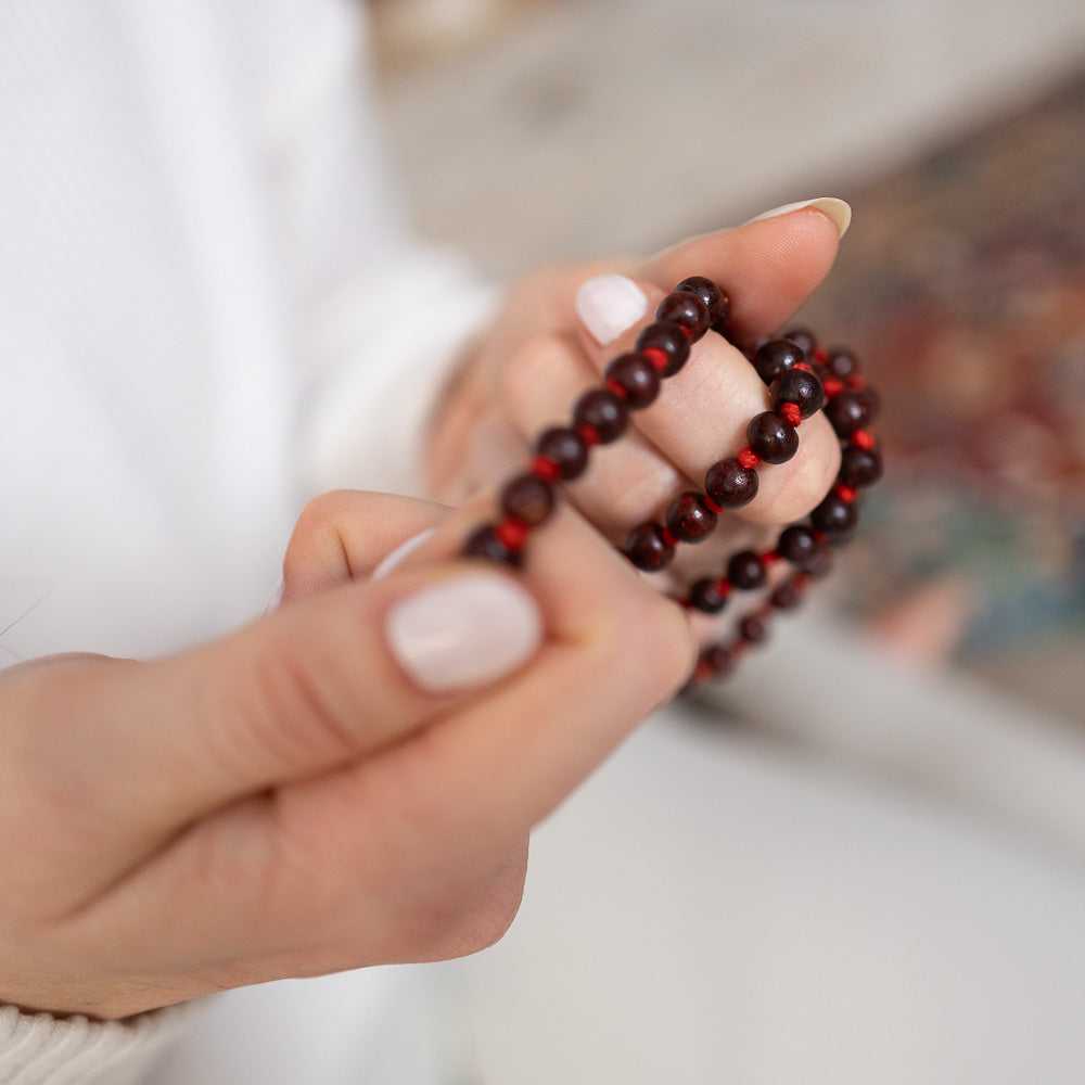 A person mindfully holding the MSY Mala Meditation Beads Rosewood necklace by Maya Shanti Yoga.