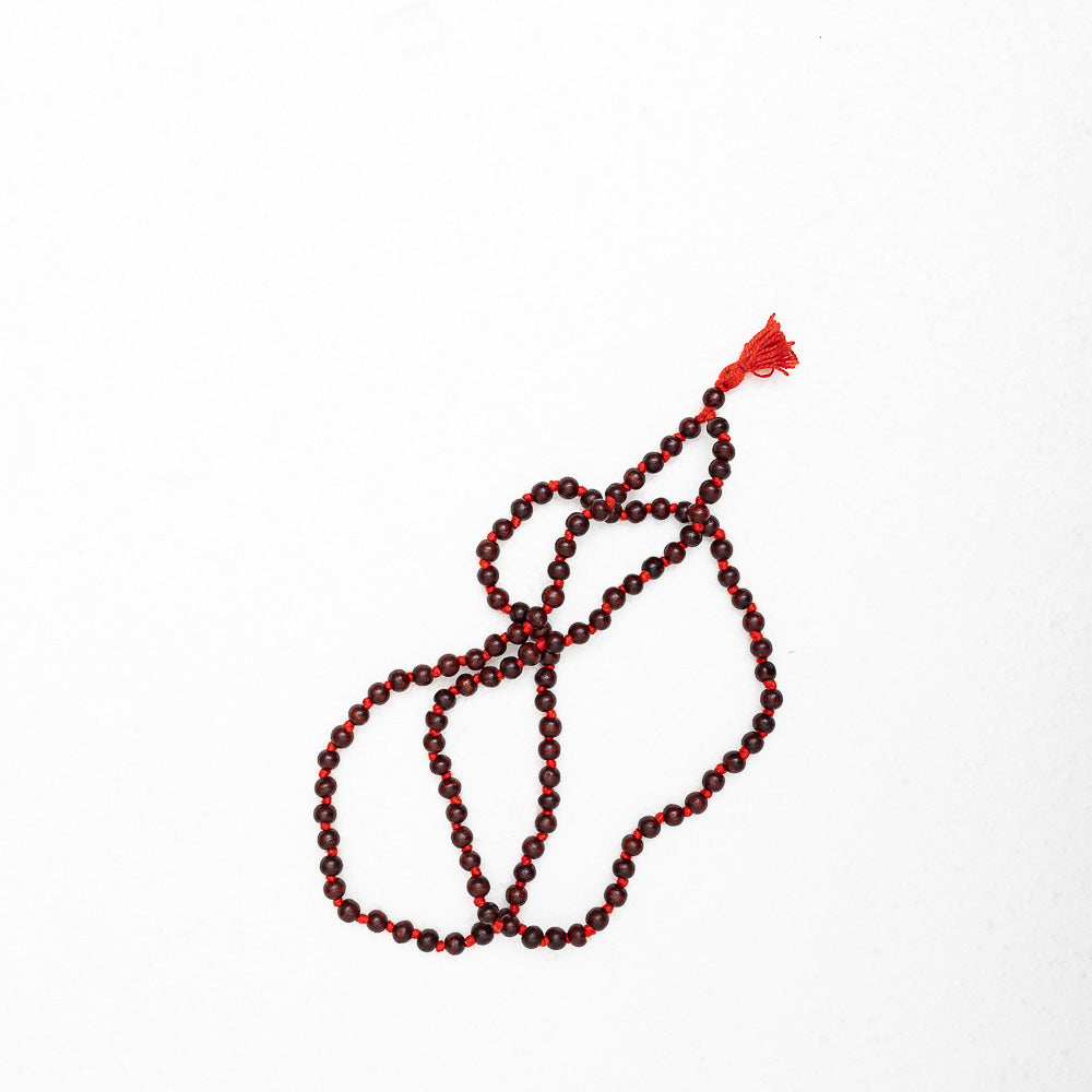 A red and brown Maya Shanti Yoga Mala Meditation Beads Rosewood resting on a white surface.