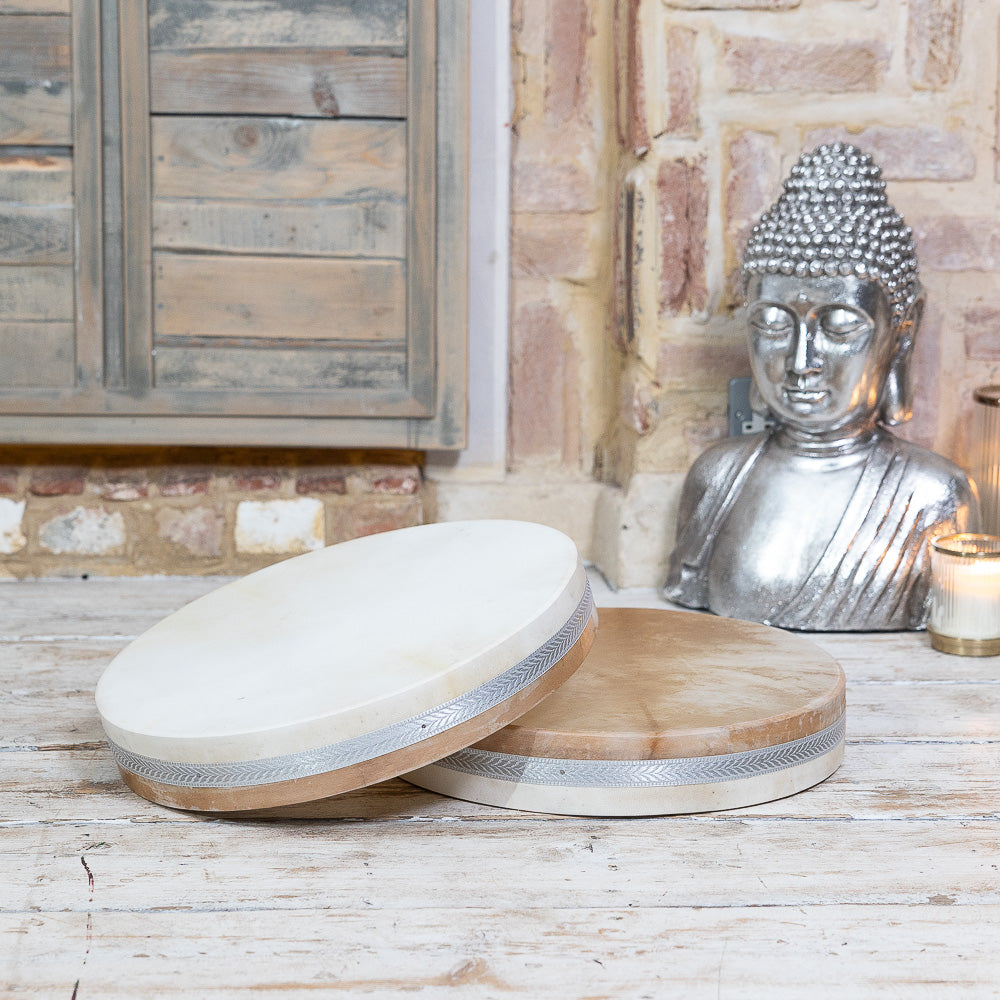 A pair of MSY Ocean Drums - 18inch by Maya Shanti Yoga on a table next to a statue, creating a serene atmosphere for meditation.