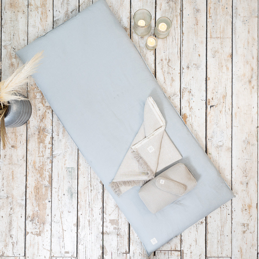 A blue MSY Shiatsu Meditation Bed - Organic Cotton by Maya Shanti Yoga placed on a wooden floor, providing the perfect space for wellness and meditation practices such as pilates.