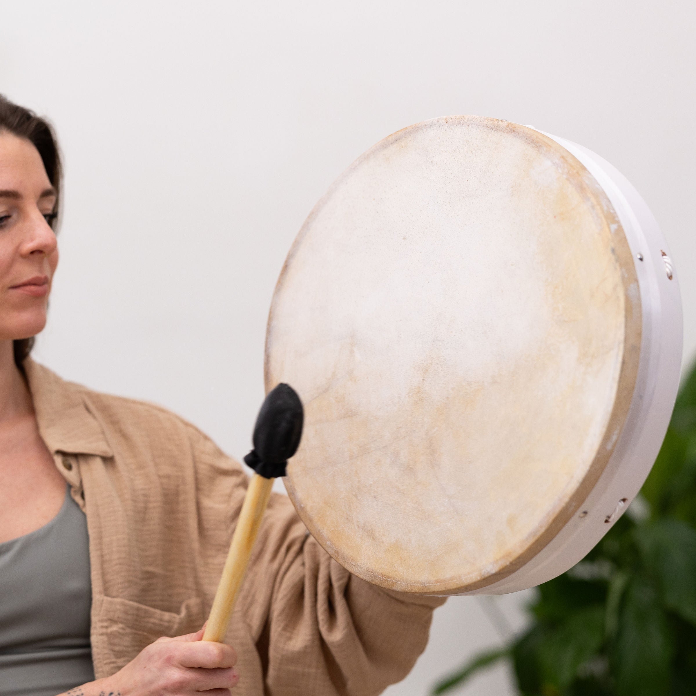 Woman holding MSY Buffalo Drum and drumstick, looking towards it with a soft expression.