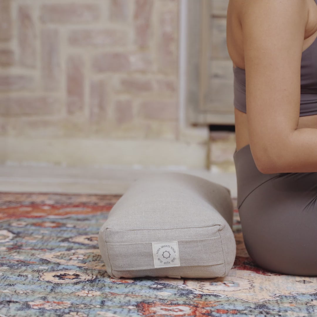 A woman practicing restorative yoga by reclining on a Maya Shanti Yoga Small Rectangular Bolster - Hemp & Buckwheat.