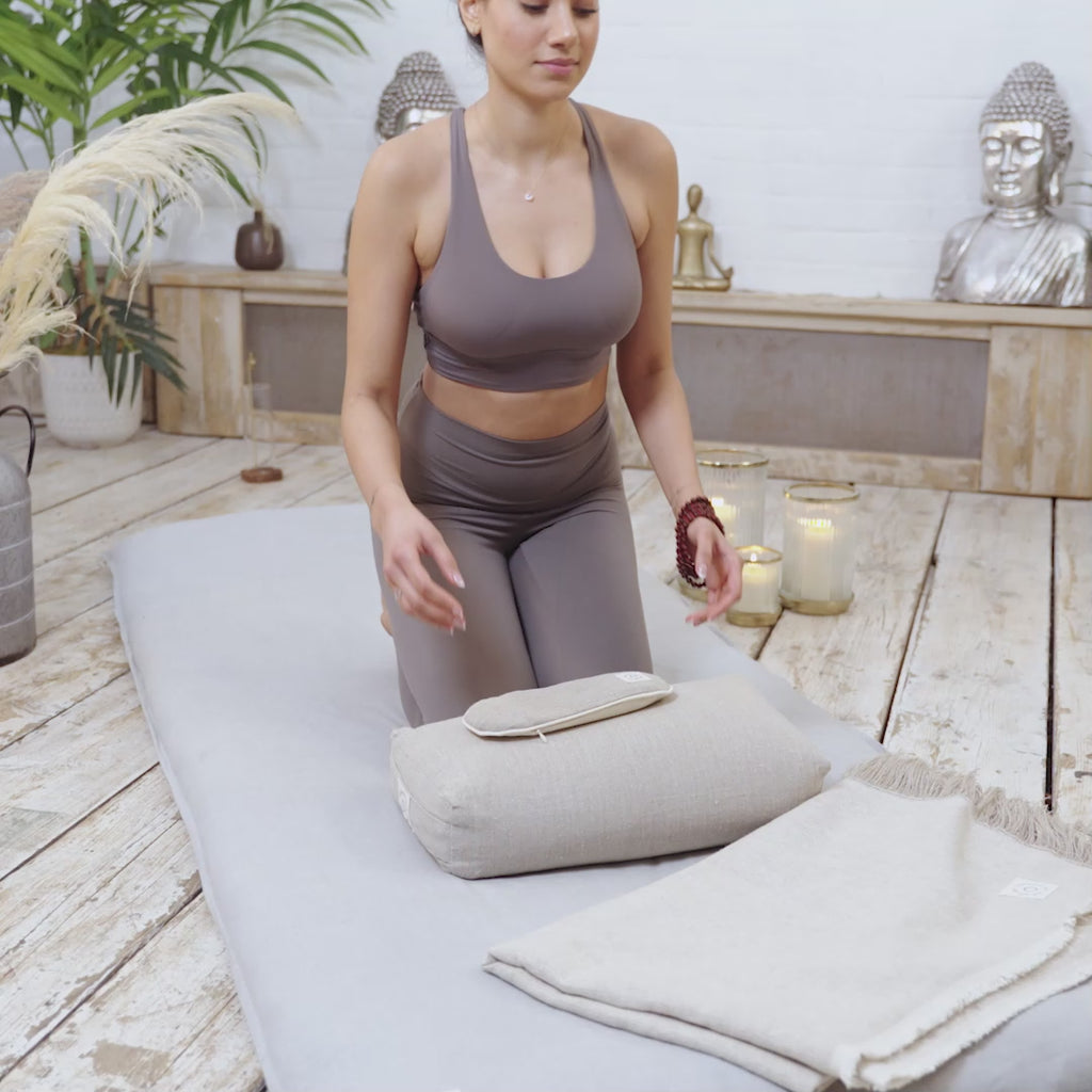 A video of a woman using Maya Shanti Yoga Tranquility Bundle pillows and blankets on a wooden floor for meditation and mindfulness.