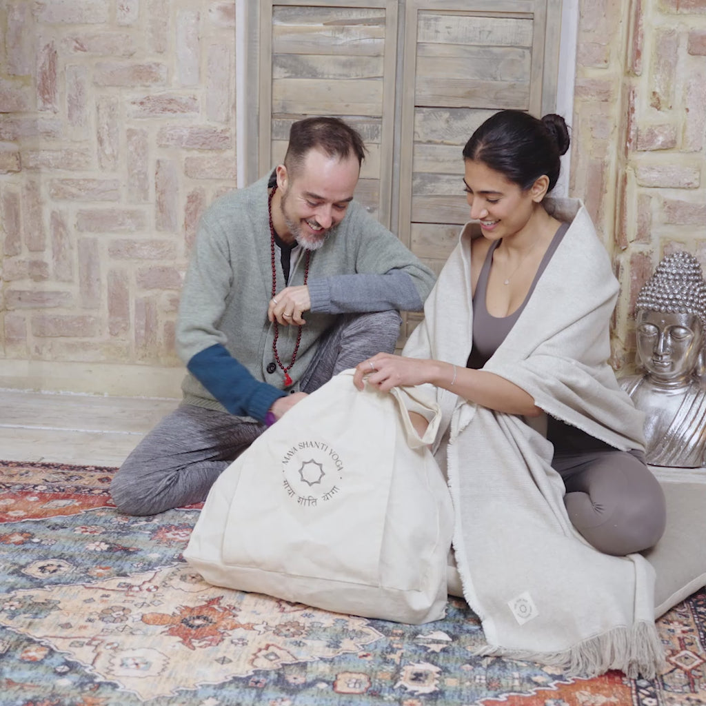 A video of A man and woman smiling and talking while sitting on a rug with a Maya Shanti Yoga Totebag - Cotton with a built-in yoga mat holder.