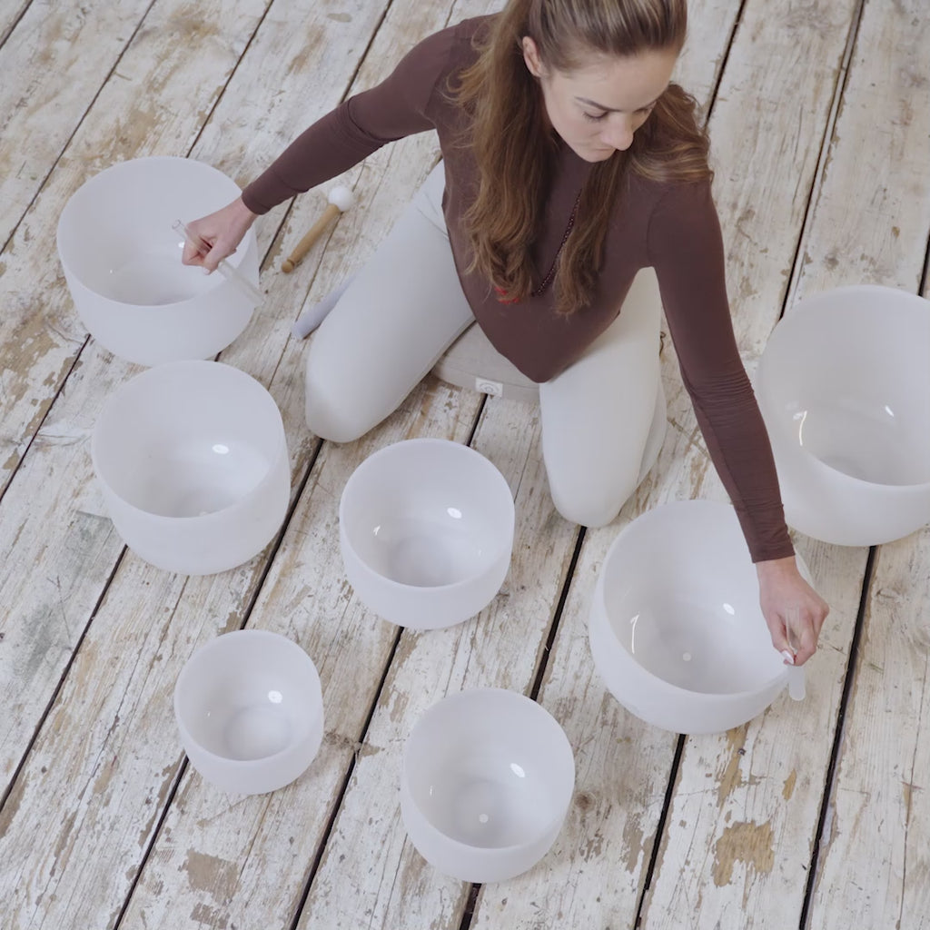 A video of a woman practising mindfulness by playing Crystal Singing Bowls- by Maya Shanti Yoga on a wooden floor.